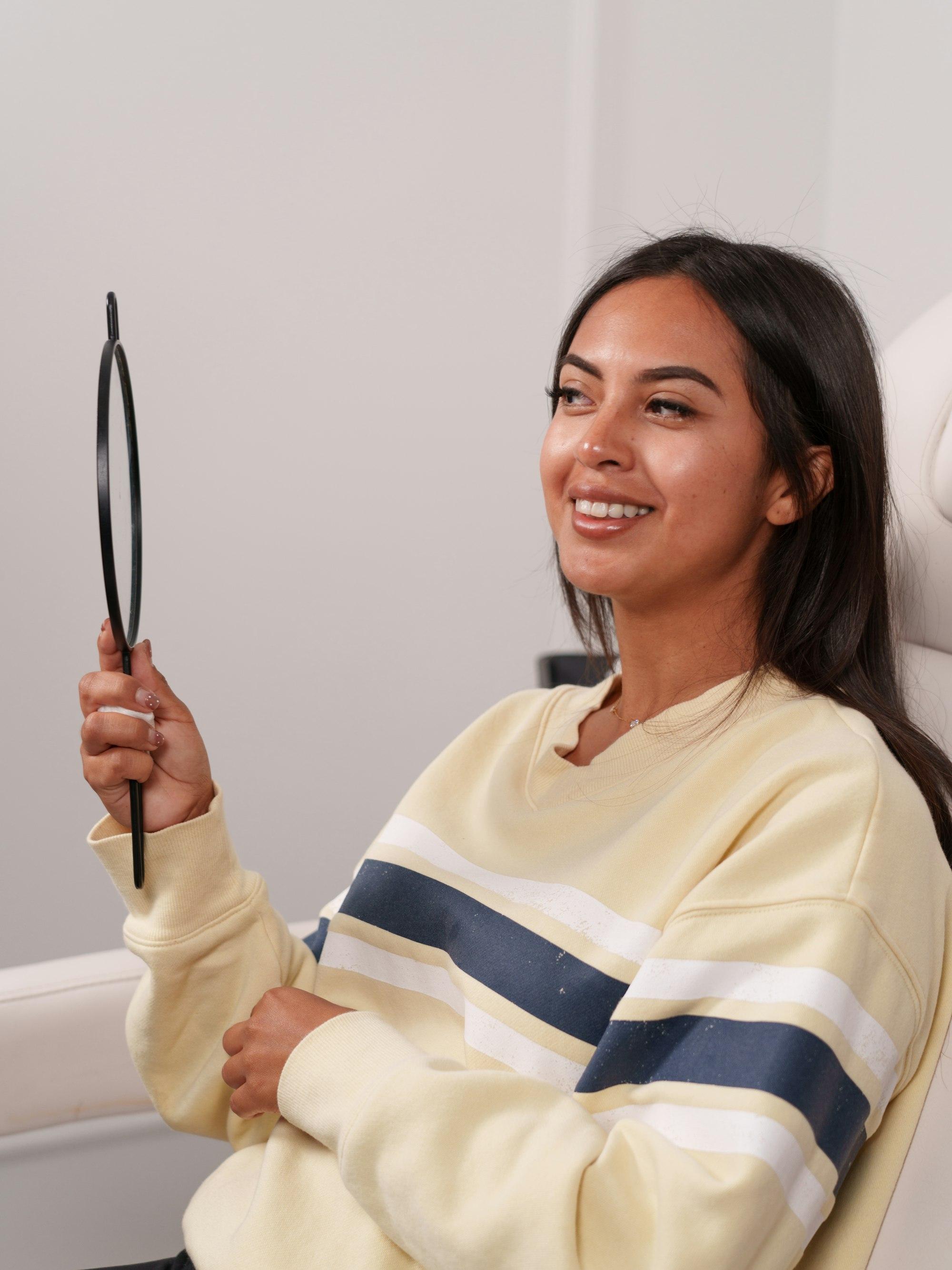 Smiling patient in a dental chair checking her smile in a hand mirror